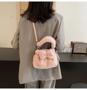 Detail of pink plush bucket bag featuring large bow and heart-shaped metal buckle on strap
