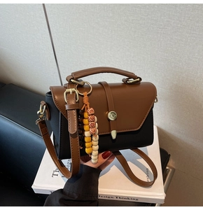Détail du sac bicolore avec texture tissée, pompon en perles de bois et fermoir doré