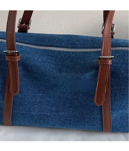 Detail of blue denim barrel bag featuring brown leather trim and silver metal zipper