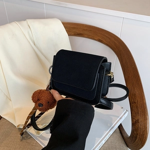 Minimalist black square crossbody bag with brown bear charm on a wooden chair