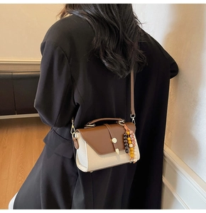 Détail du sac bicolore avec rabat en cuir marron et breloque perlée porté par un modèle