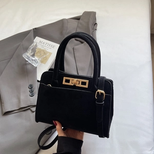 Detailed close-up of matte black suede handbag featuring golden rectangle twist lock and hardware