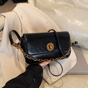 Vintage black shiny leather crossbody bag with gold chain and circular lock on blazer