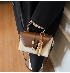 Détail d'un sac à main bicolore en toile avec poignée en cuir et pompon en perles ethniques