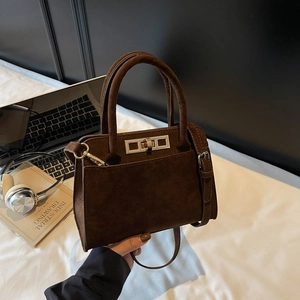 Close-up of a dark brown suede handbag featuring a metal twist lock and cylindrical handle