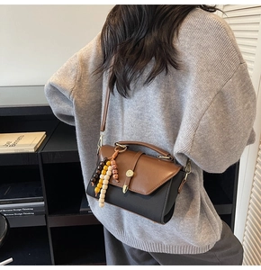 Détail du sac à bandoulière bicolore avec rabat marron et breloque décorative en perles