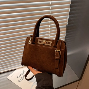 Close-up of dark brown suede handbag with golden buckle and sleek leather top handle