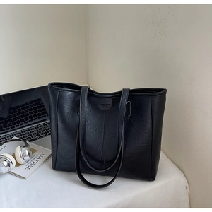 Dettaglio della borsa tote nera in pelle martellata sulla scrivania con accessori vari
