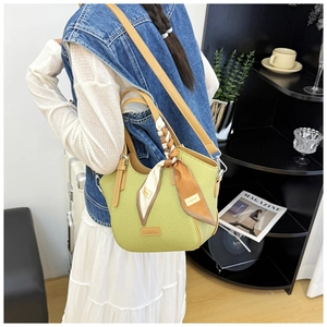 Detail of light green woven handbag with brown leather straps and stylish silk scarf accessory