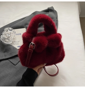 Detail of burgundy plush bucket bag with fuzzy pom-poms and adjustable leather strap