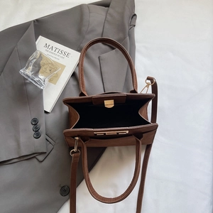 Detail of a brown matte suede handbag with gold hardware next to a gray blazer