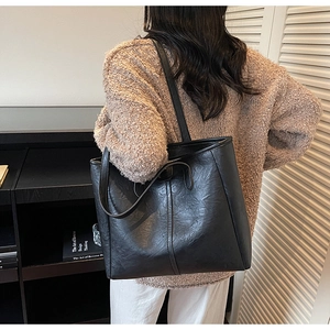 Dettaglio di una grande borsa tote nera con trama in pelle plissettata su una modella