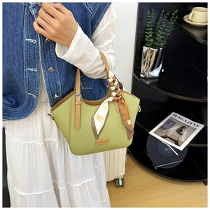Detailed close-up of woven light green handbag with brown leather handle and floral scarf