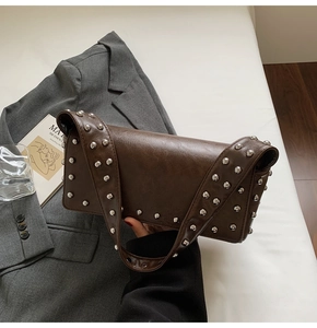 Detail of dark brown leather shoulder bag with silver rivet studs on a grey blazer