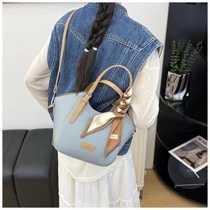 Detail of light blue textured handbag with brown leather handle and printed silk scarf