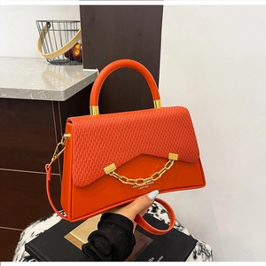 Détail du sac à main trapèze orange avec rabat tissé et chaîne métallique dorée