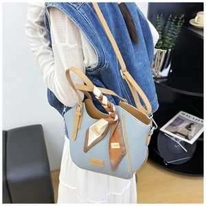 Detail of light blue woven tote bag featuring brown leather handles and a silk scarf accent
