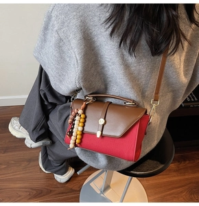 Détail du sac bandoulière avec breloque en perles et fermoir rotatif porté par un mannequin