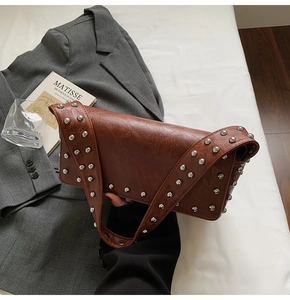 Detailed close-up of brown faux leather shoulder bag with silver rivet studs on soft bedding