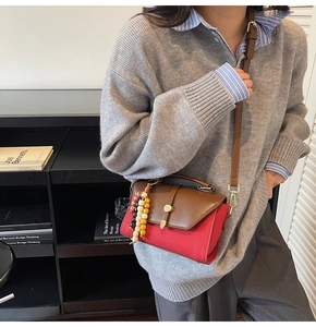 Détail d'un sac en toile rouge avec bandoulière en cuir brun et pendentif en bois
