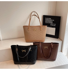 Three elegant tote bags in brown and black leather with gold bow details on marble