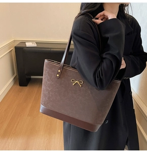 Detail of a dark brown tote bag with a golden bow ornament and smooth matte texture