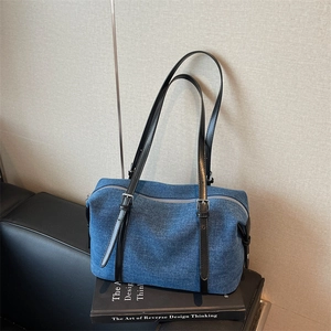 Blue denim underarm bag with black leather strap on a decorative book setting