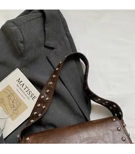 Detailed shot of dark brown shoulder bag with silver rivets on wide strap and flap