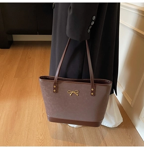 Detail of vintage brown leather tote bag featuring a golden metal bow fastener and texture