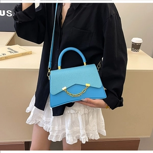 Détail d'un sac bleu vif avec rabat à texture tressée et chaîne dorée élégante