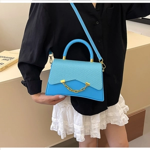 Détail d'un sac bandoulière bleu vif avec chaîne dorée et texture tissée sur mannequin