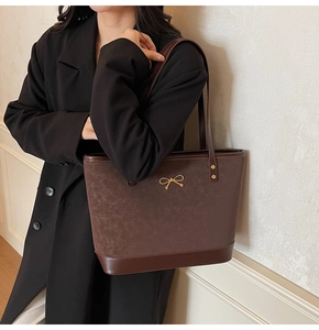Detail of brown leather tote bag with gold bow ornament and dark trim on black coat