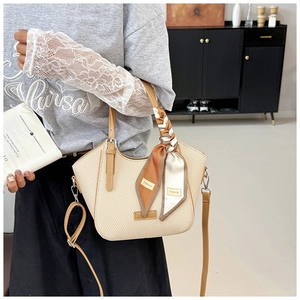 Detail of beige woven tote bag with brown leather handles and decorative silk ribbon
