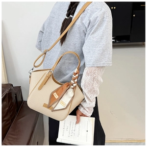 Detail of beige woven tote bag with brown leather handles and a silk scarf accessory
