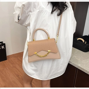 Modèle portant un sac bandoulière beige avec rabat tissé et chaîne dorée