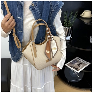 Detail of woven crossbody bag with brown leather handles and decorative silk scarf