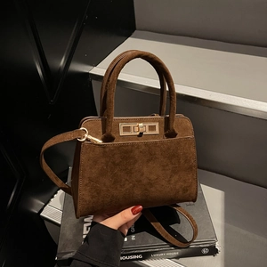 Vintage brown suede tote bag with golden clasp and adjustable strap on a dark background