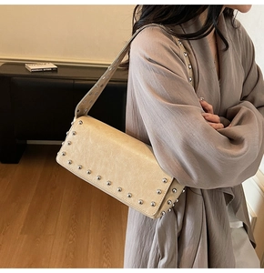 Detail of vintage beige underarm bag with silver rivets worn by model in a cozy interior