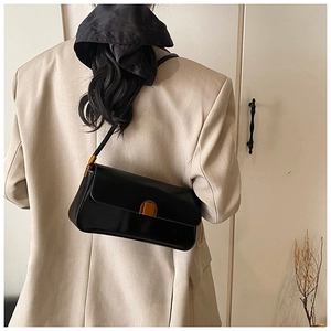 Classic black baguette shoulder bag with gold hardware worn over the shoulder by a model