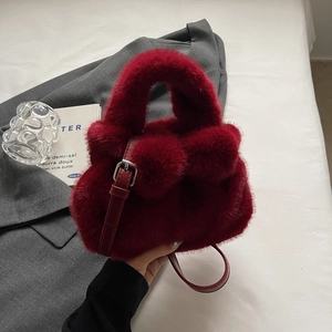 Deep red plush faux fur bucket bag with decorative pom-poms and adjustable strap