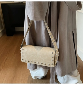 Detail of cream shoulder bag with silver studs and faux leather texture on strap
