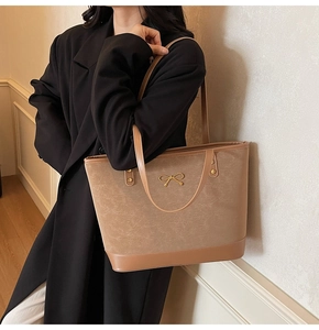 Detail of a brown tote bag featuring a metallic bow buckle and matte leather texture