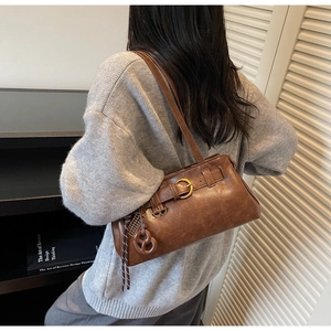 Macro detail of dark brown leather Boston bag with gold buckle and pretzel charm accent