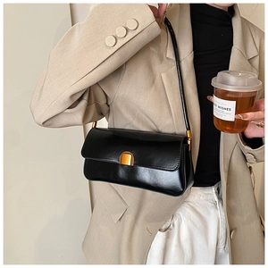 Detail of black glossy leather baguette bag with gold and wood buckle on a beige blazer