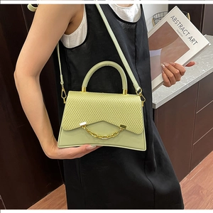 Sac bandoulière vert clair avec rabat tressé et chaîne dorée tenu par un modèle