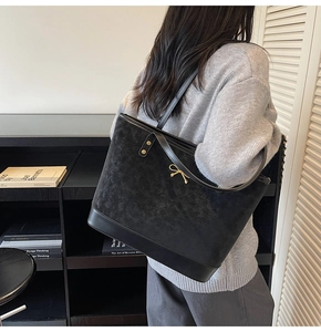 Detail showing a black tote bag with gold metal hardware and smooth leather stitching