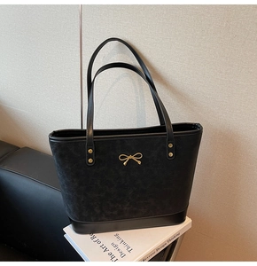 Detail showing the mixed-texture black tote bag with a golden bow buckle on the front