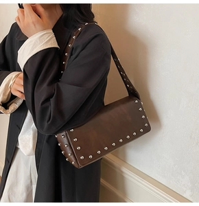 Detail of dark brown shoulder bag with silver rivet studs and a wide strap in retro style