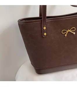 Detail of dark brown tote bag showing matte texture and golden bow hardware accents