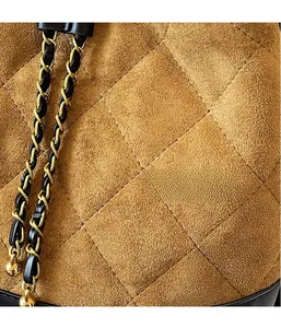 Macro detail of brown suede bucket bag featuring diamond quilting and gold chain strap